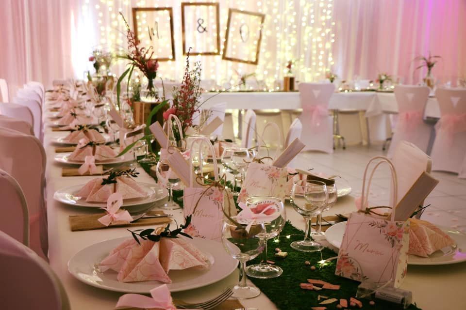 Table de banquet dressée avec un décor rose et or, des assiettes blanches et des centres de table floraux.