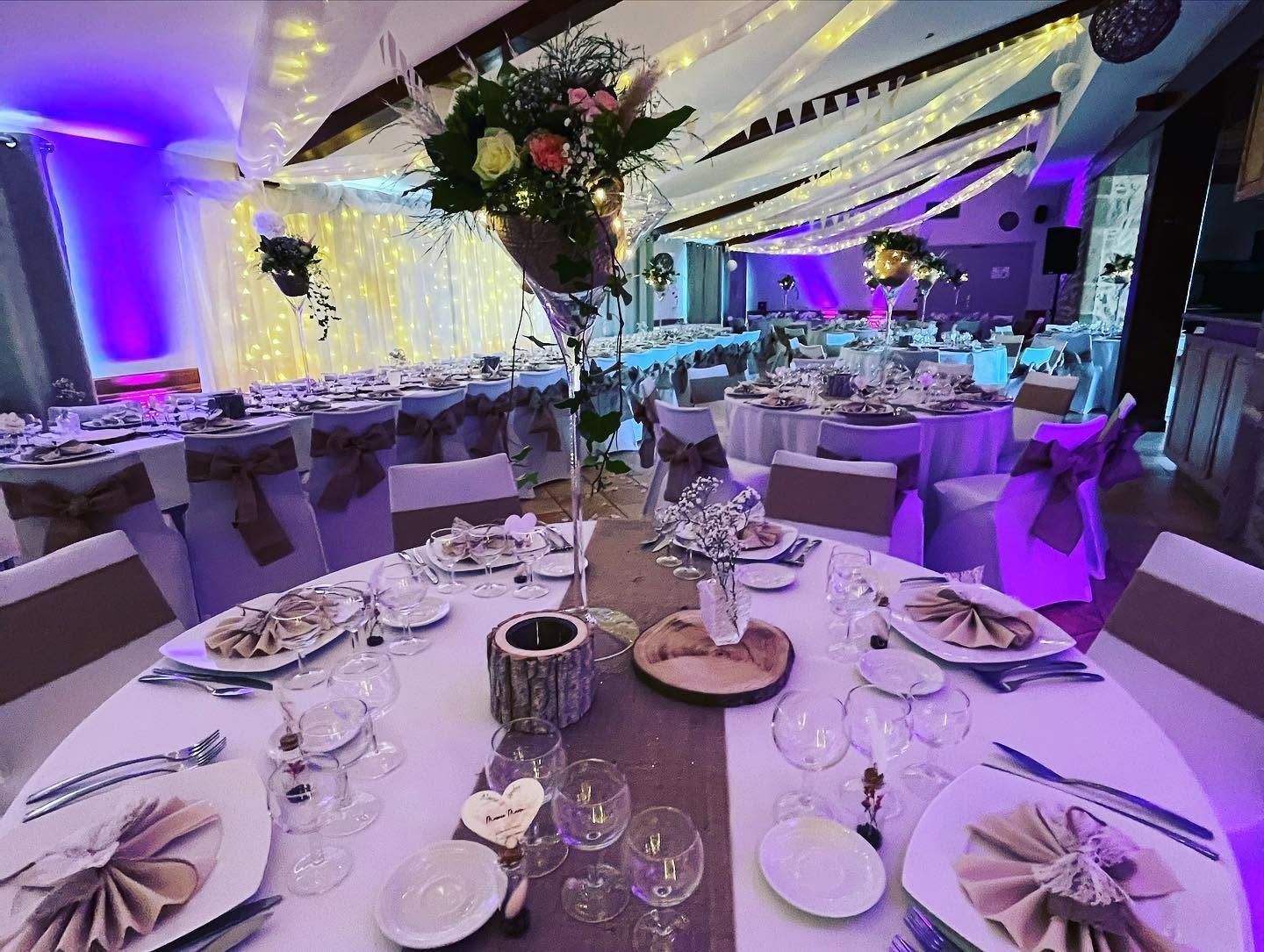 Salle de réception avec tables rondes et des décorations florales, illuminée dans des tons de violet.