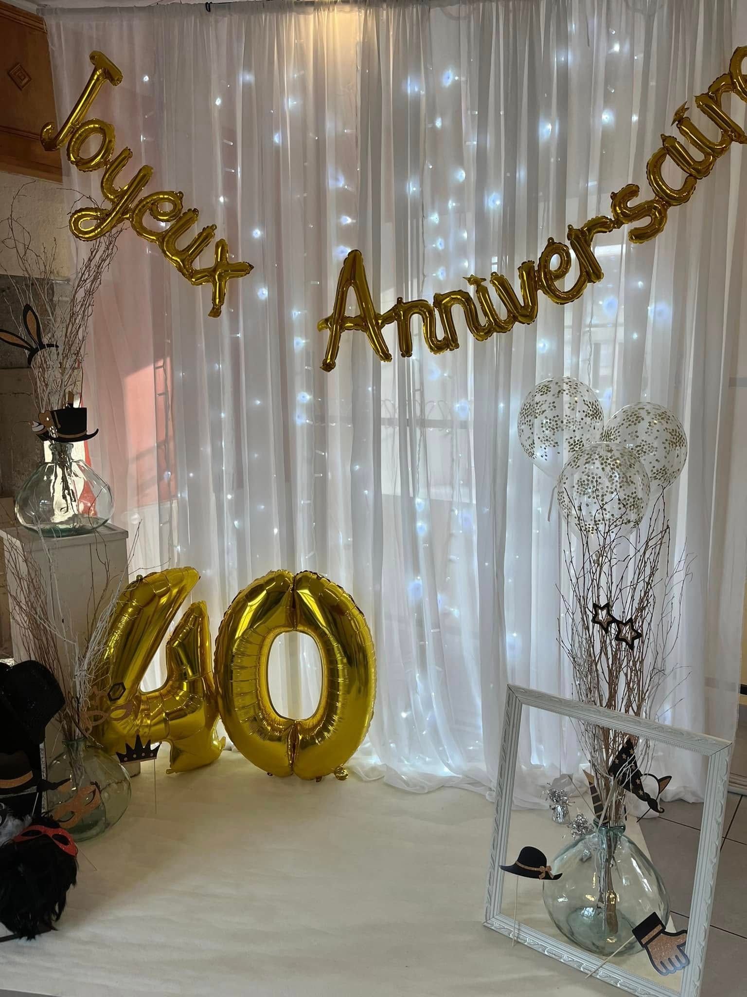 Décor pour une fête d'anniversaire avec des rideaux blancs, des guirlandes lumineuses et de grands ballons dorés.