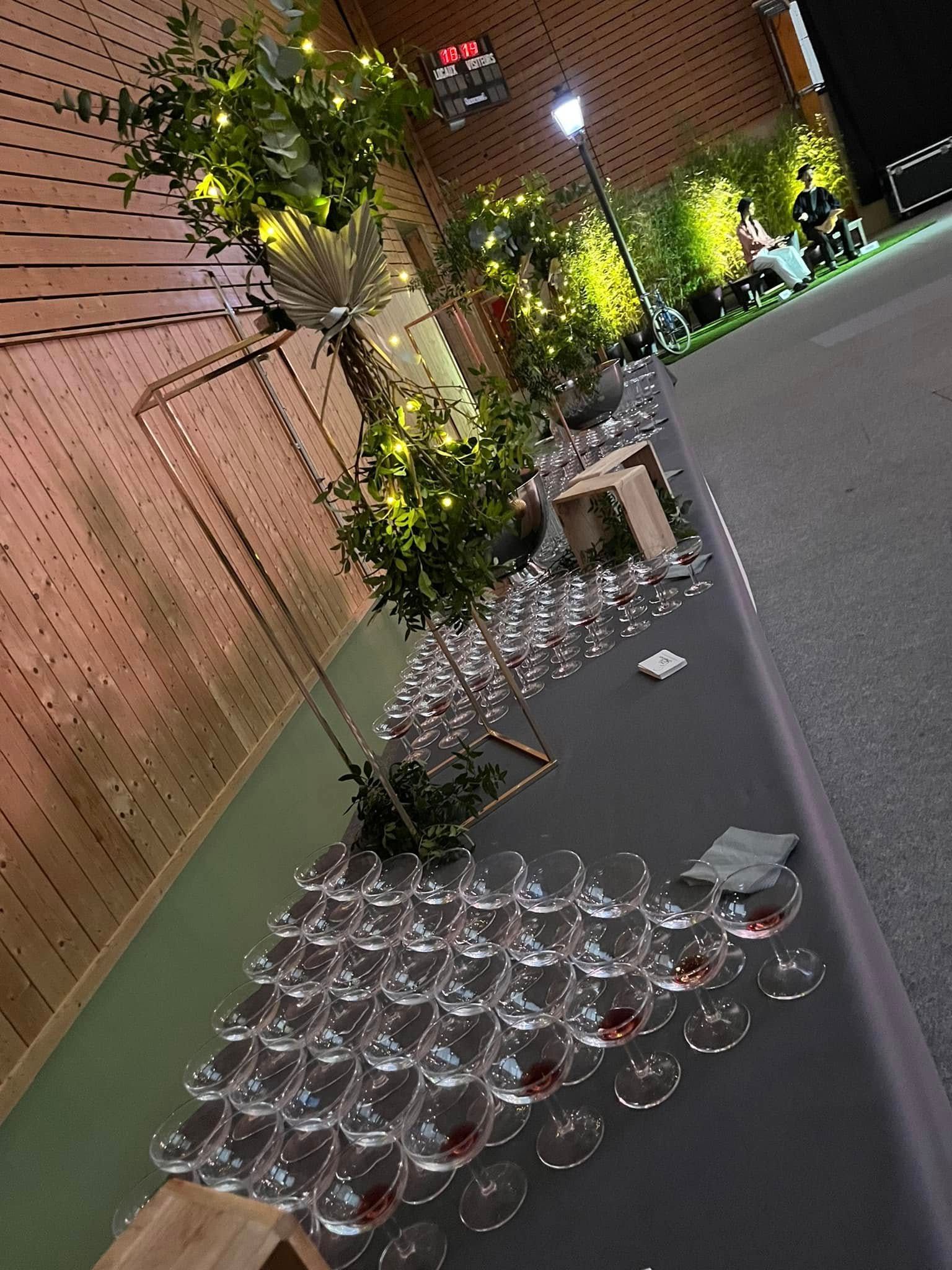 Une longue table dans une salle avec des verres posés dessus et de la décoration végétale.