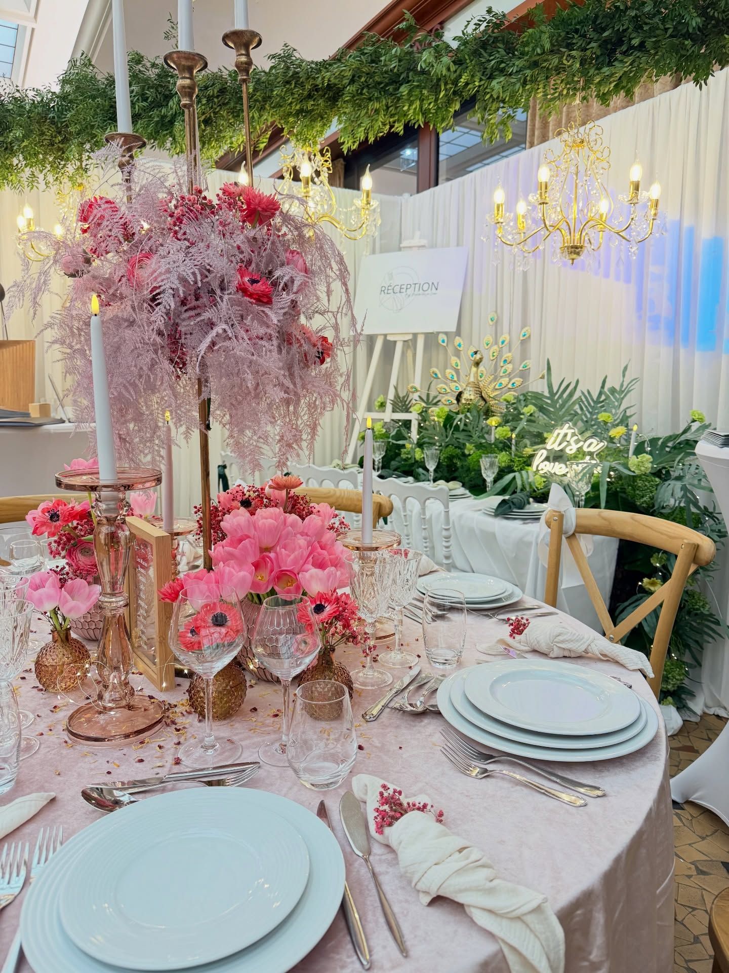 Élégante table de banquet rose à motifs floraux, avec des assiettes blanches et des bougies.