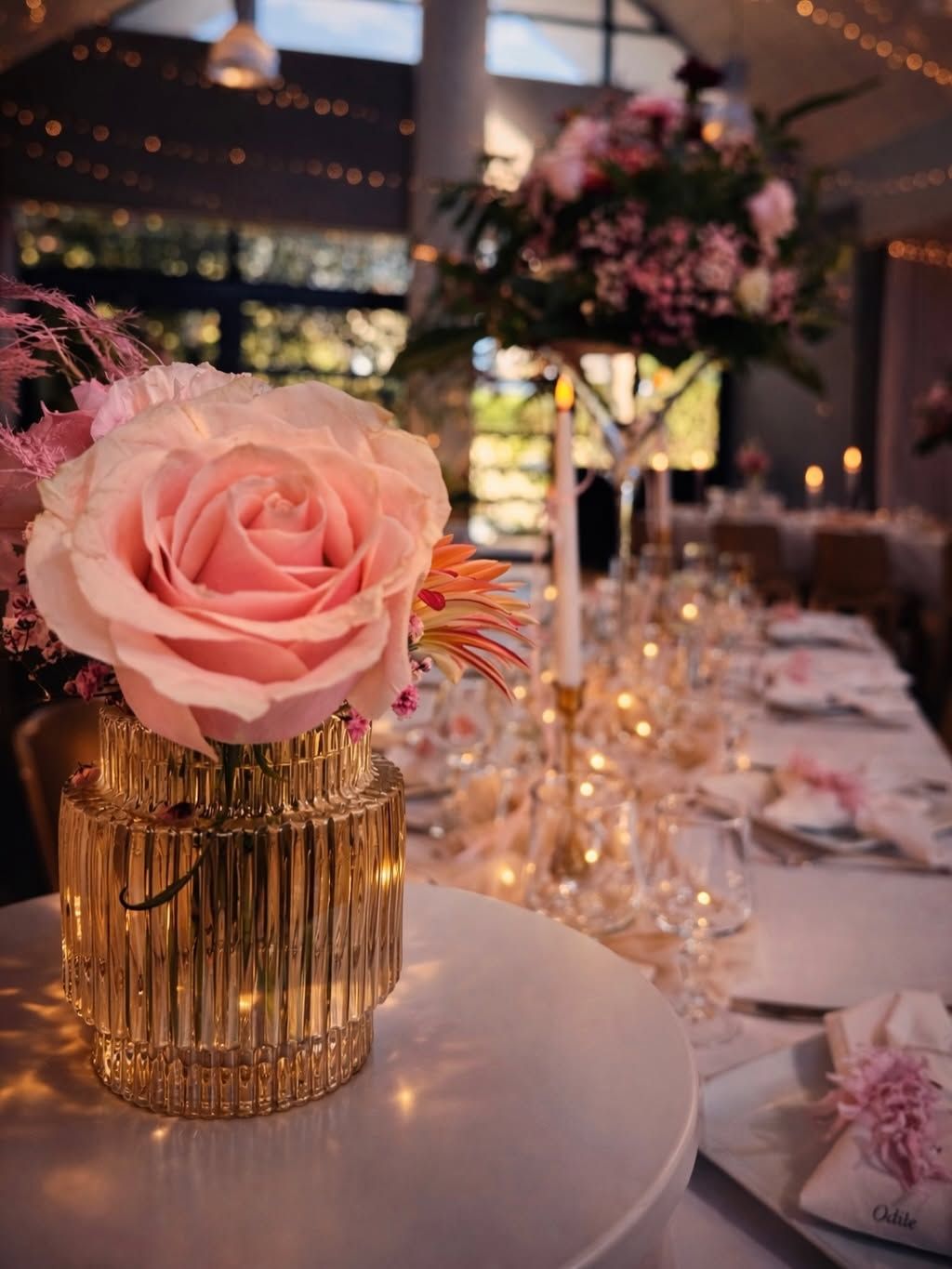 Centre de table composé de roses dans un vase doré, sur une table de banquet éclairée ornée de décorations florales.