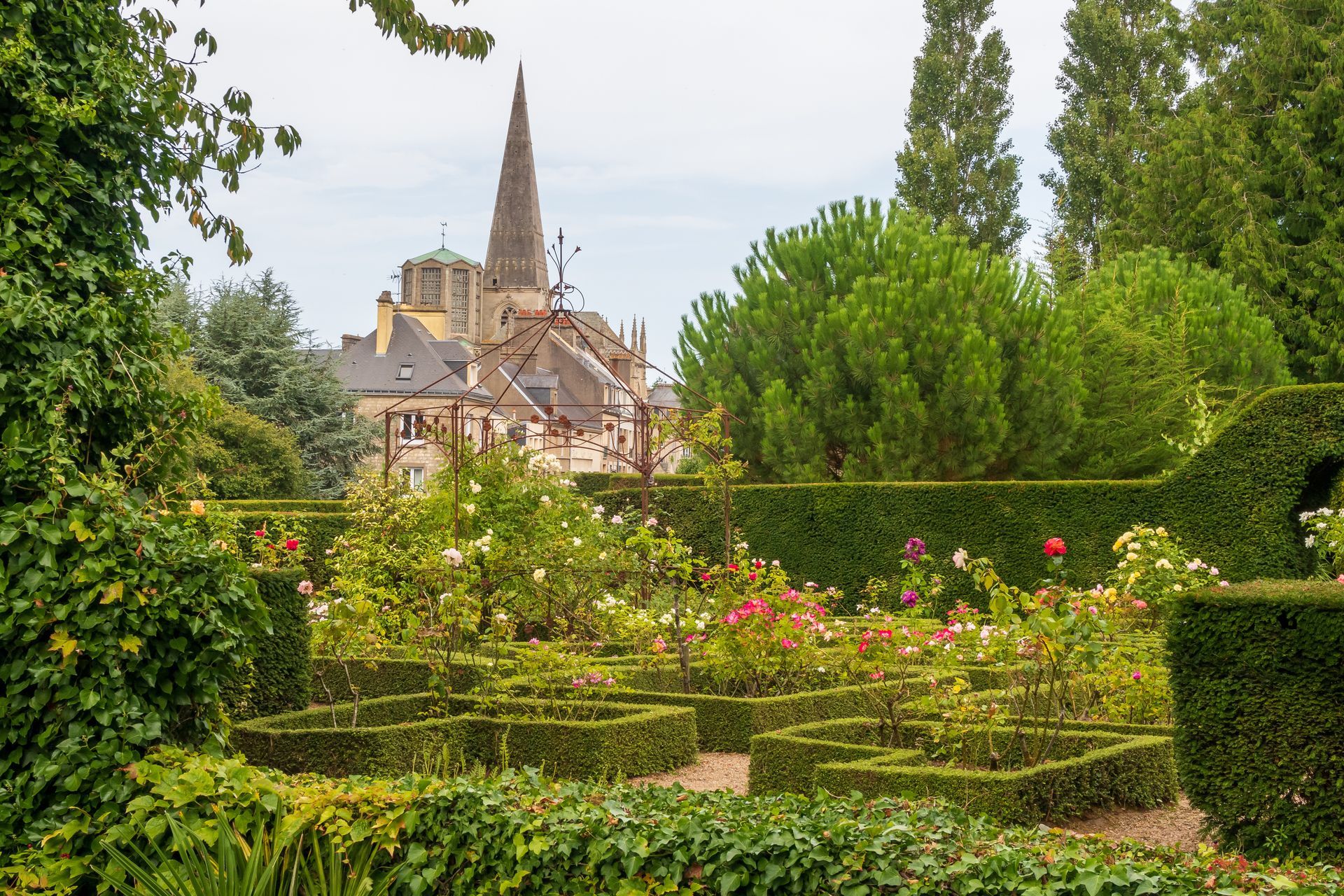 Vue de l'église de Valognes depuis des jardins verts.