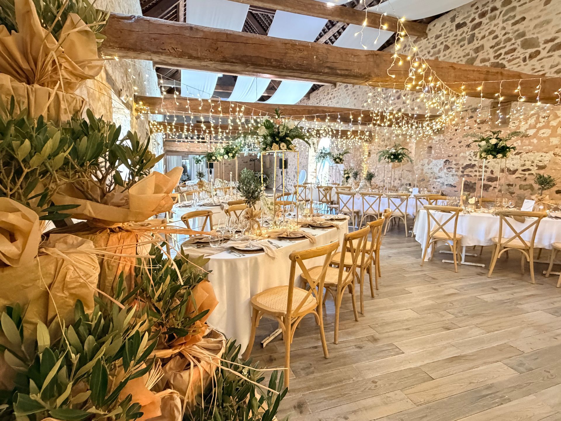 Salle de réception décorée de fleurs blanches, de tables et de chaises en bois et de guirlandes lumineuses.