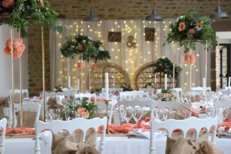 Élégante salle de banquet avec tables blanches, centres de table floraux et guirlandes lumineuses.