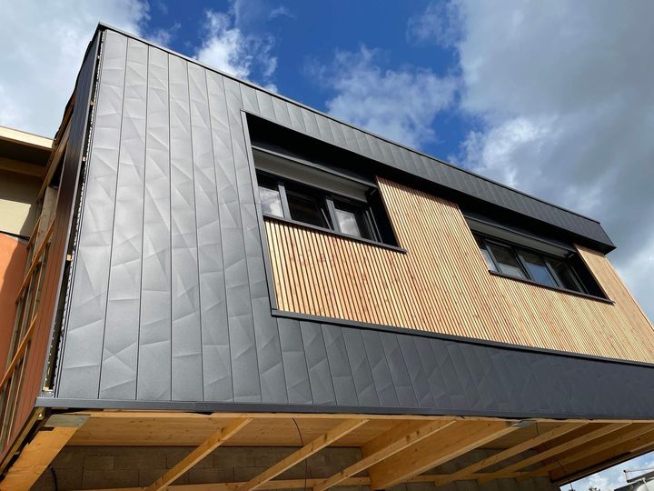Extérieur d'une maison moderne avec un revêtement en métal foncé, des lambris et un ciel bleu au-dessus.