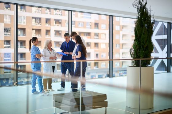 Quatre personnes discutent dans le hall lumineux d'un immeuble de bureaux, près d'une balustrade en verre et de grandes fenêtres.