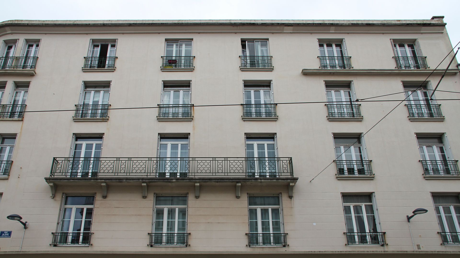 Façade d'un immeuble d'appartements beige avec des rangées de fenêtres et de balcons.