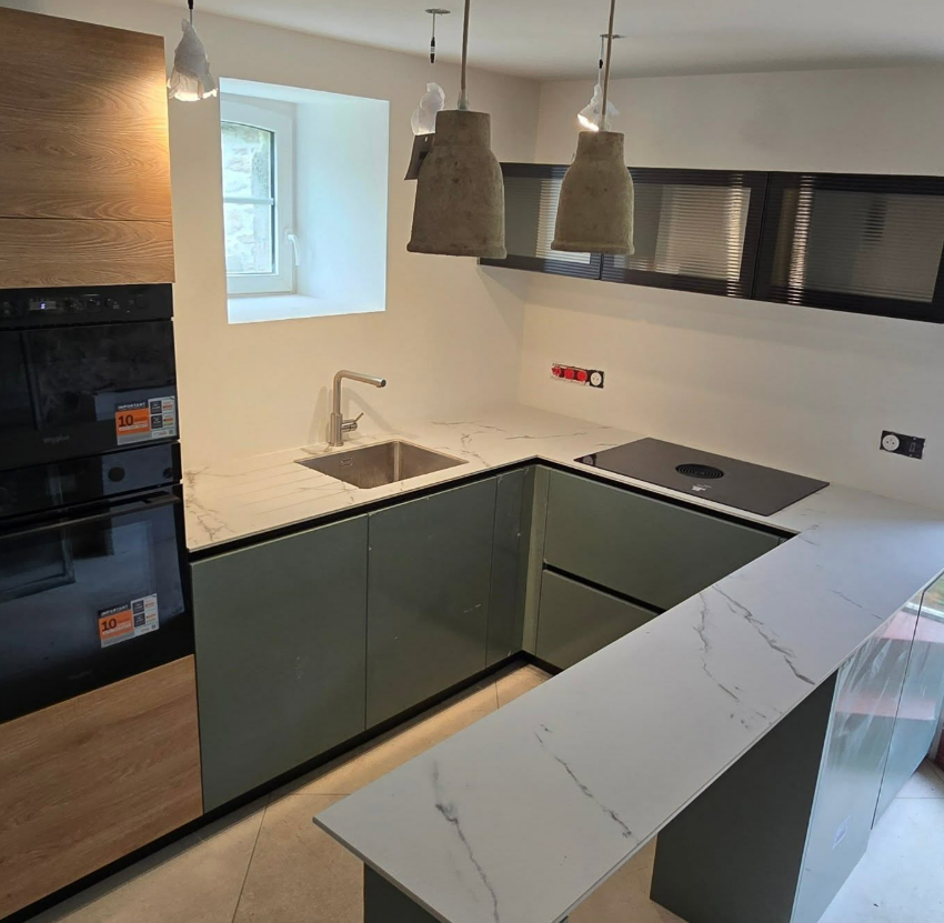 Cuisine moderne avec un plan de travail blanc, des placards verts, des luminaires suspendus et un évier.