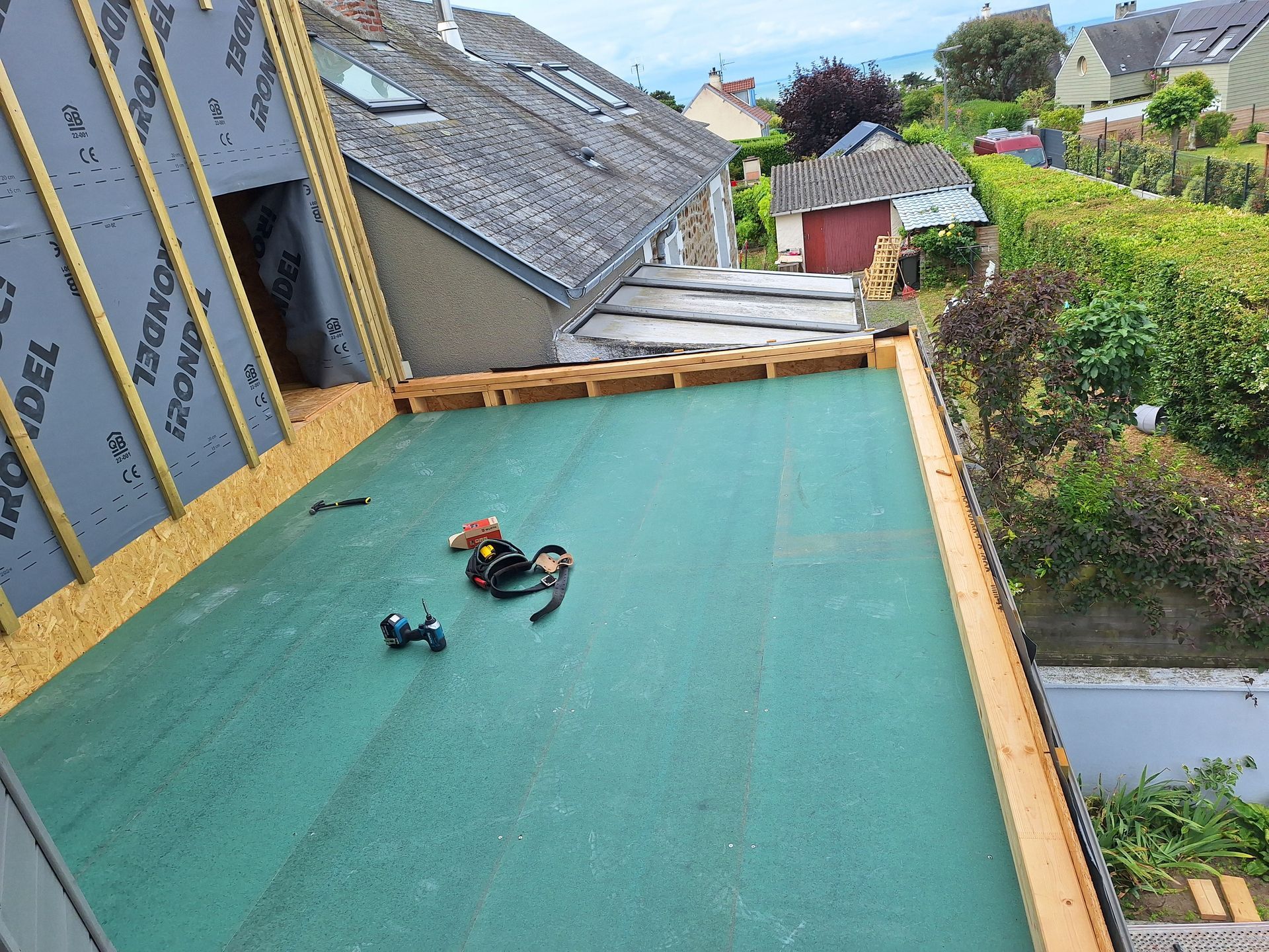 Toiture plate en construction avec matériau de toiture végétalisée, ossature en bois et outils.
