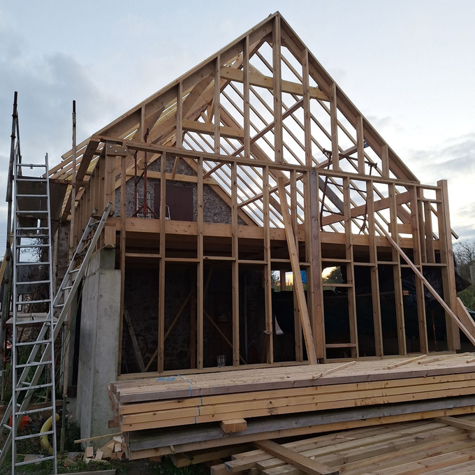 Maison à ossature en bois en construction avec échelle, sur fond de ciel nuageux.