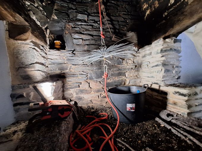 Cheminée en cours de ramonage : seau noir, brosse et suie à l'intérieur d'une cheminée en pierre.