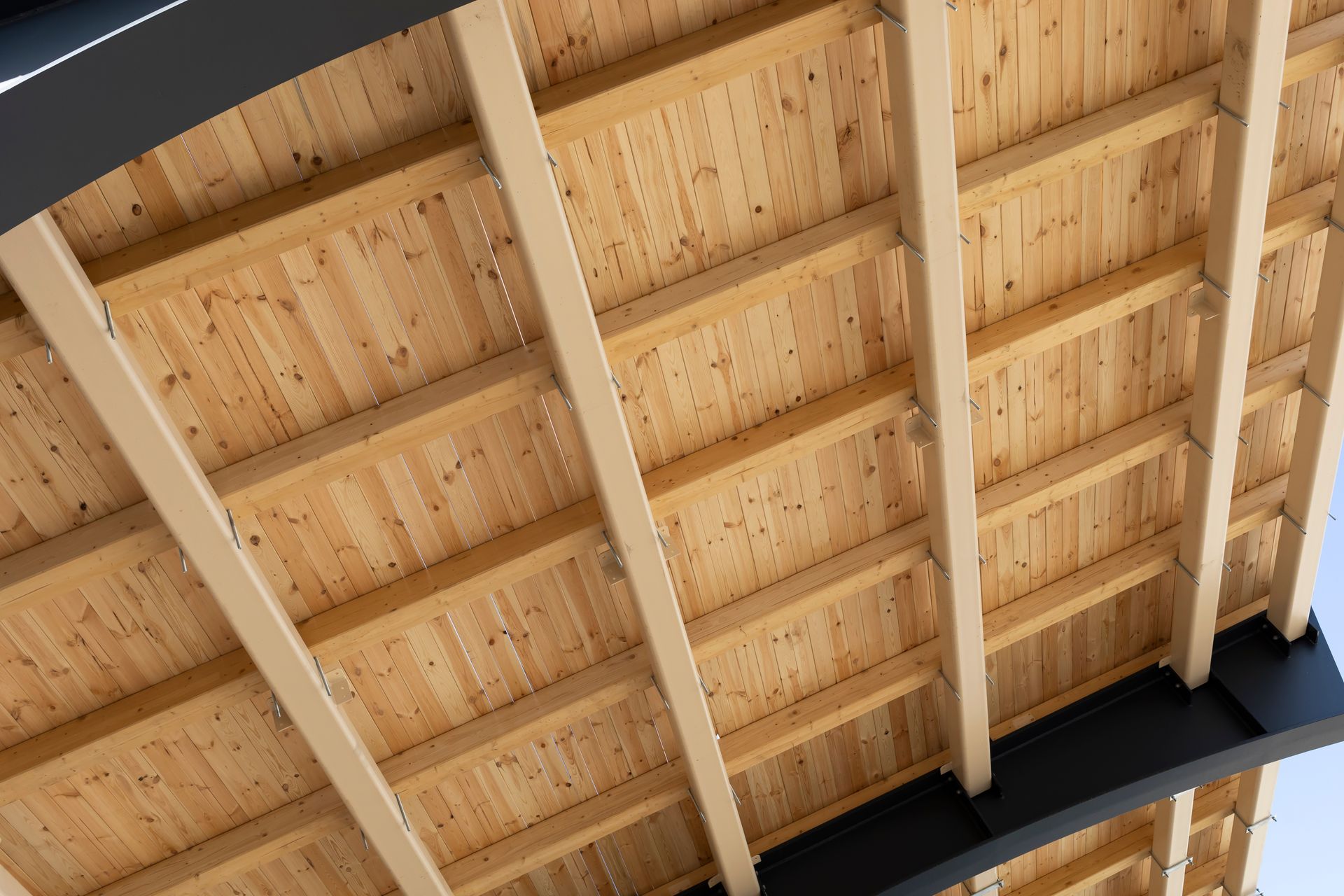 Construction de toiture en bois avec poutres apparentes, planches de bois clair et supports en métal noir.