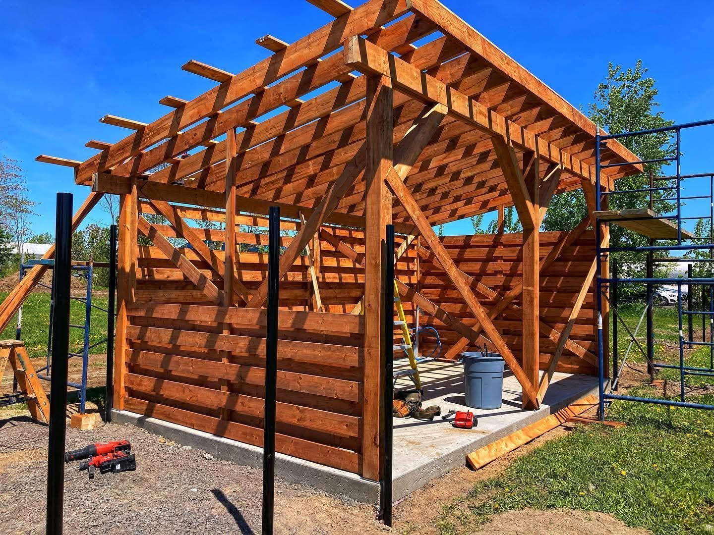 Maison à ossature en bois en construction avec échelle, sur fond de ciel nuageux.