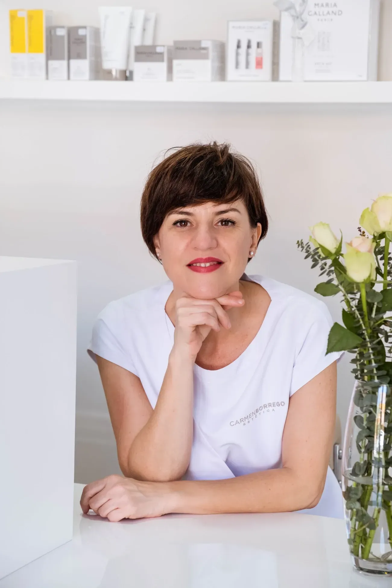 Una mujer está sentada en una mesa frente a un jarrón de flores.