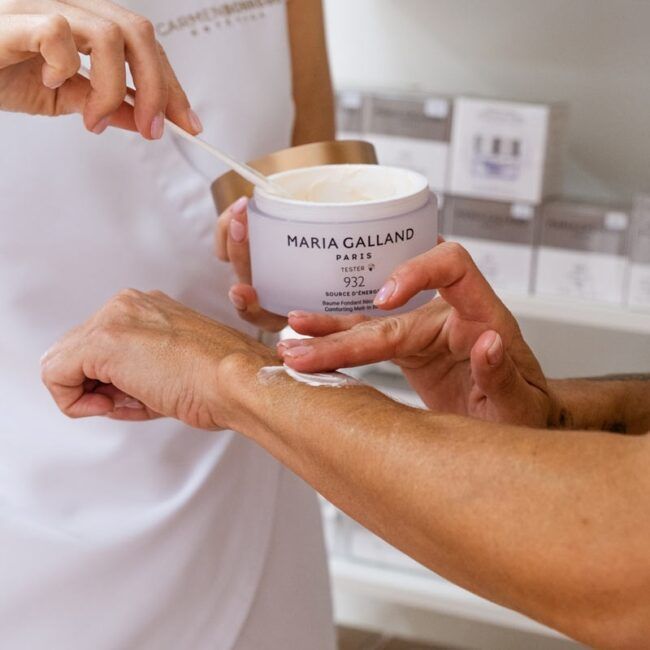 Una mujer está aplicando crema de Maria Galland Paris en el brazo de otra mujer.