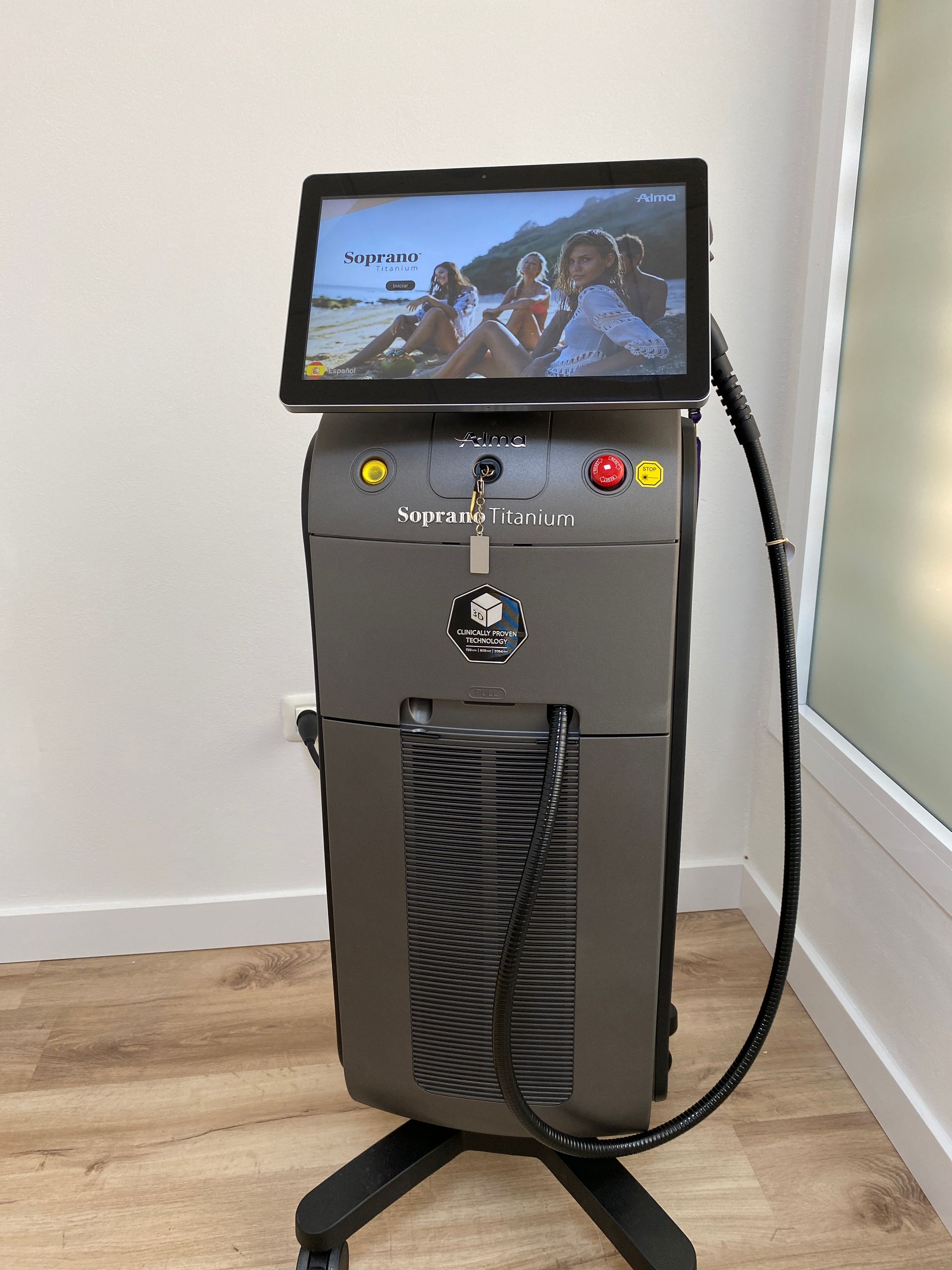 Una máquina de depilación láser de color gris oscuro con pantalla táctil y brazo flexible, cerca de una pared blanca.