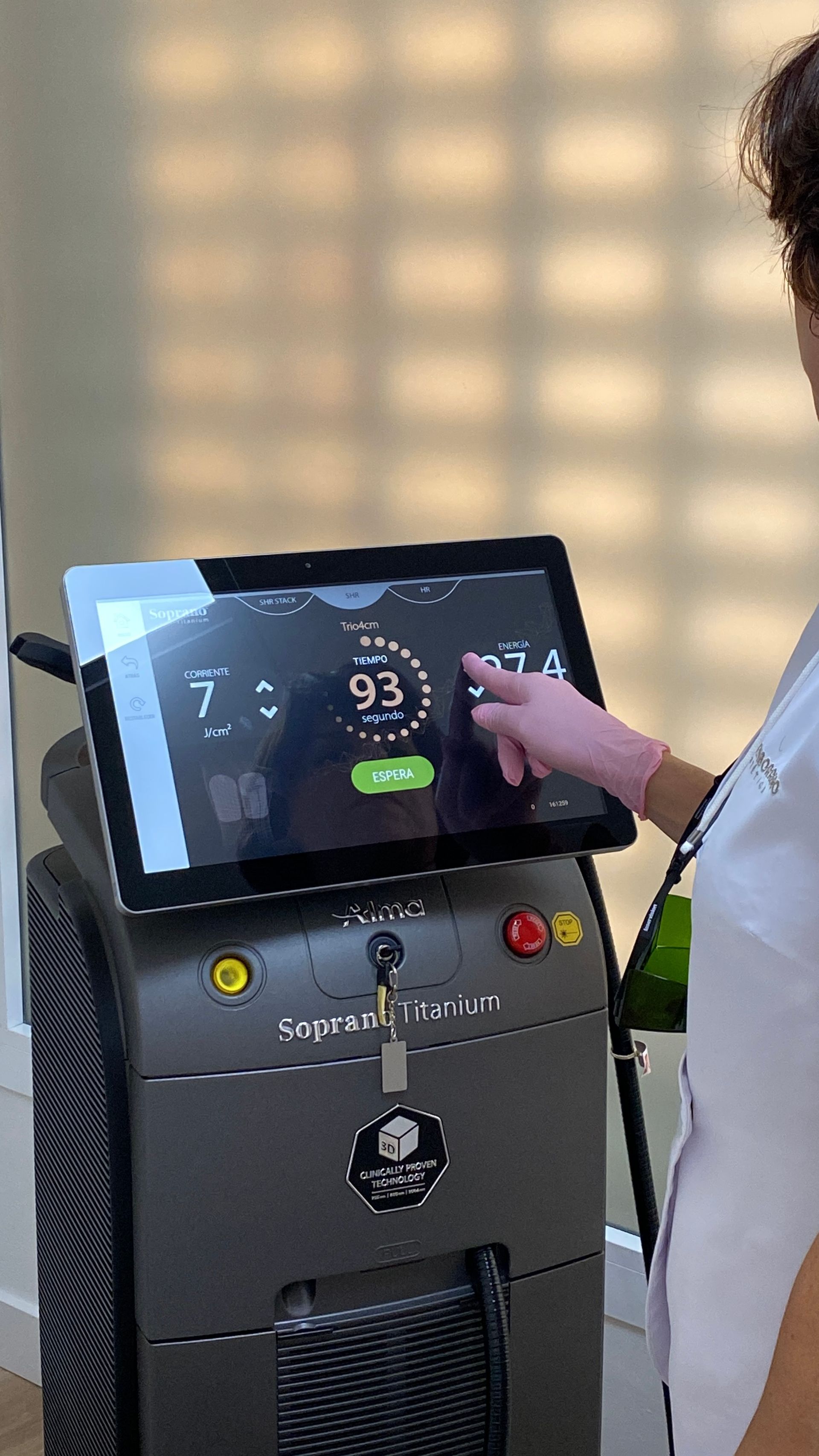 Persona tocando la pantalla de un dispositivo médico, configurado en 93, en un consultorio médico.