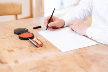 Une personne écrit sur du papier à une table en bois, à côté d'un encreur et de petits outils à tamponner.