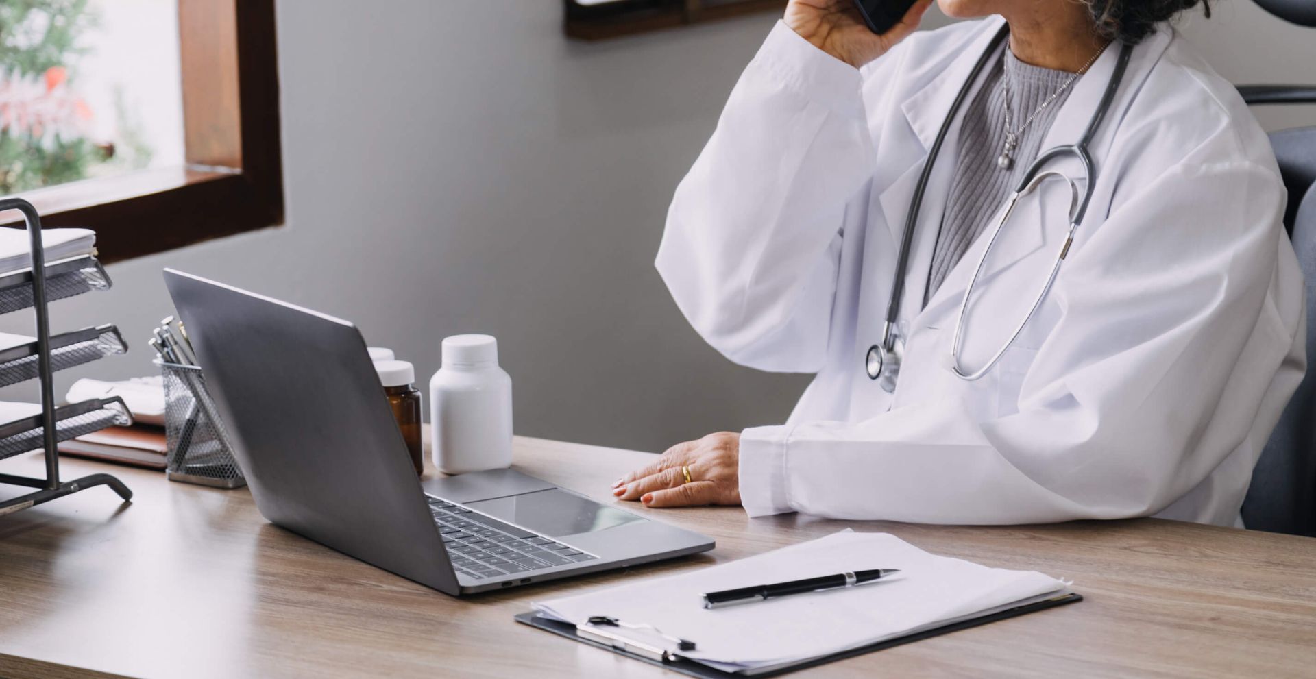 Un médico está sentado en un escritorio hablando por un teléfono celular.