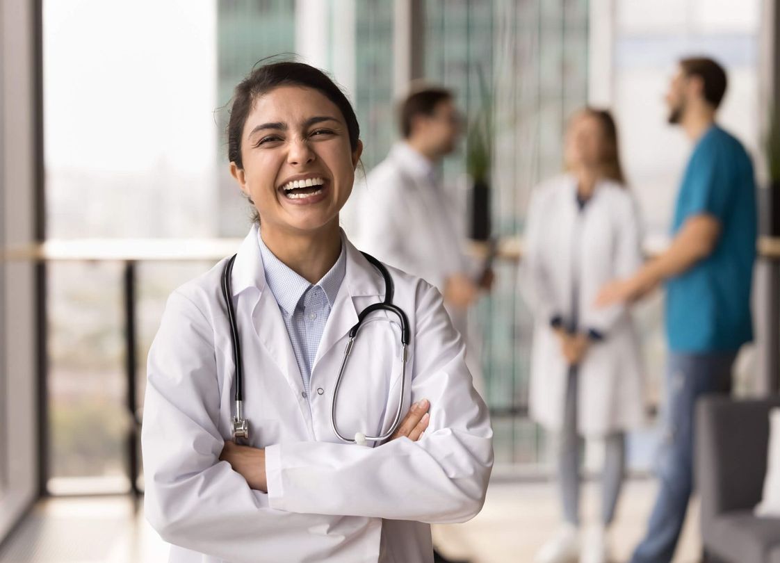 Una doctora sonríe con los brazos cruzados en el pasillo de un hospital.