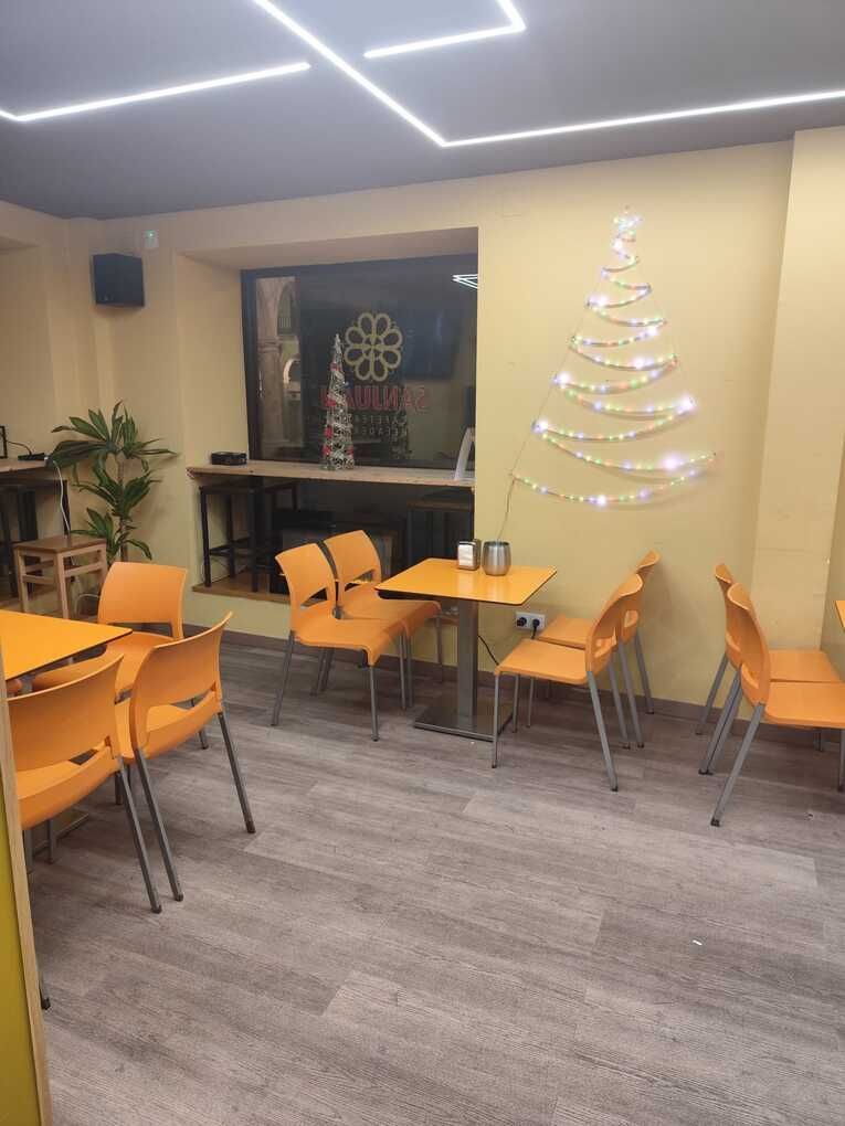 Interior de restaurante con sillas y mesas de color naranja y un árbol de Navidad con luces de cadena sobre una pared amarilla.