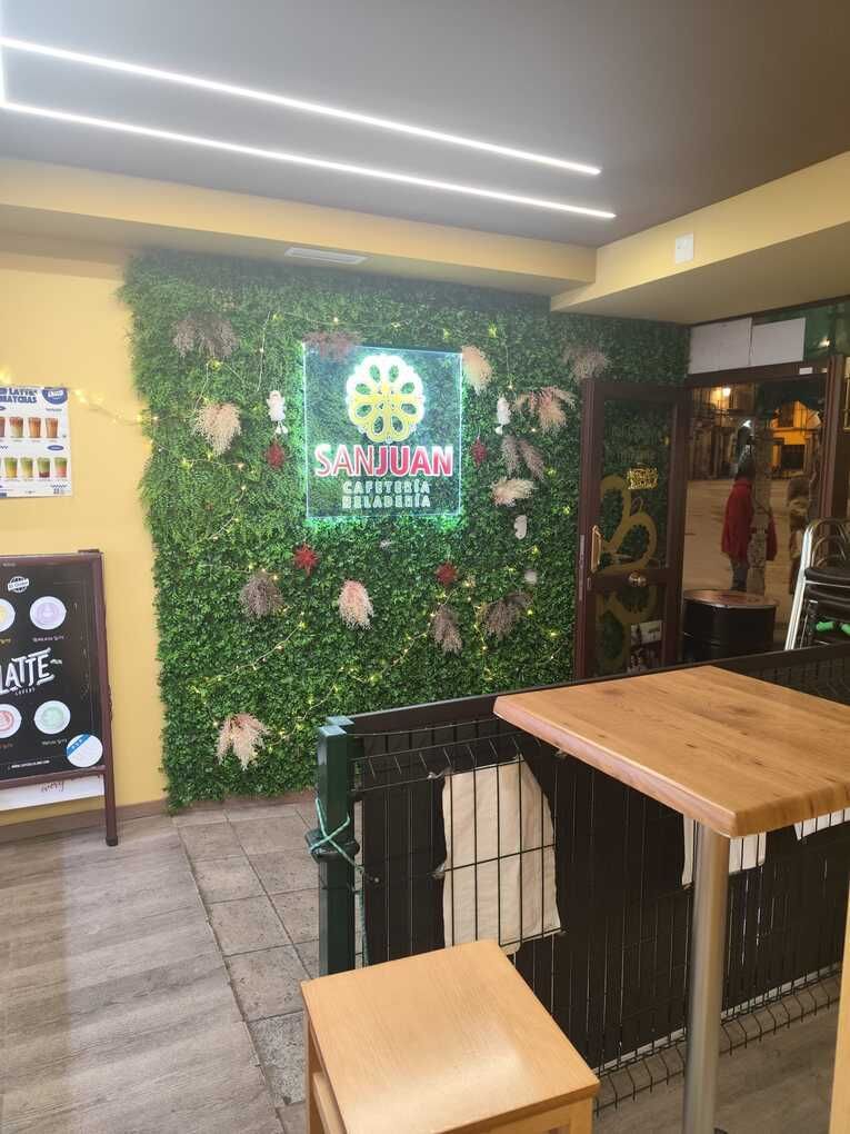 Interior de restaurante con pared verde y logotipo. Se ven mesas y una puerta abierta.