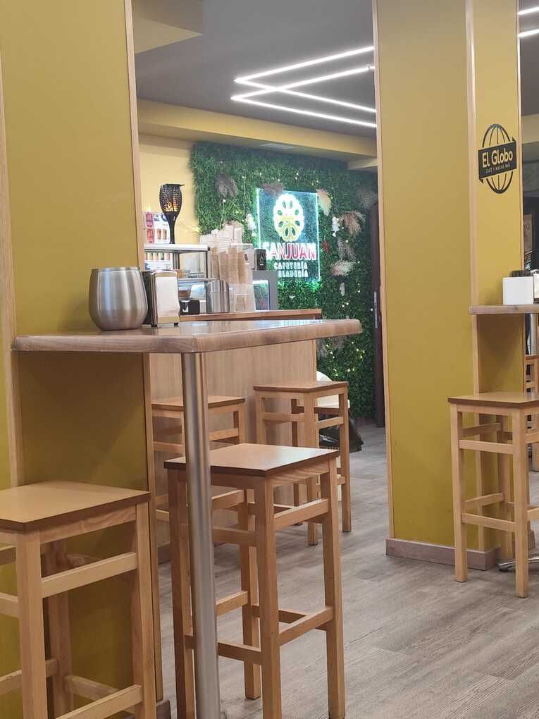 Interior de una cafetería con taburetes y mesas de madera. Pared verde, letrero de neón y paredes amarillas.