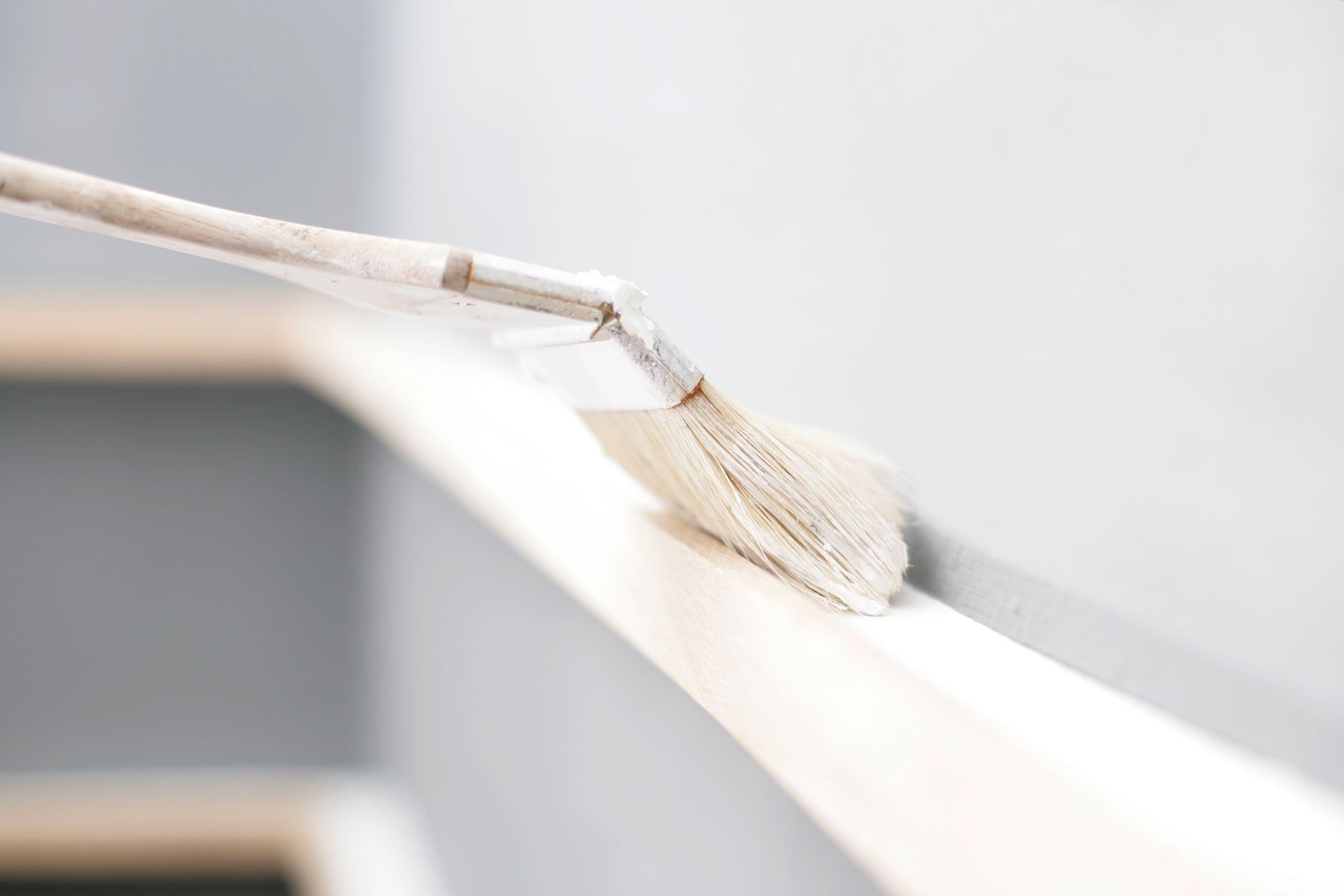 Mit einem Pinsel wird weisse Farbe an die Kante einer Wandleiste vor einer hellgrauen Wand aufgetragen.