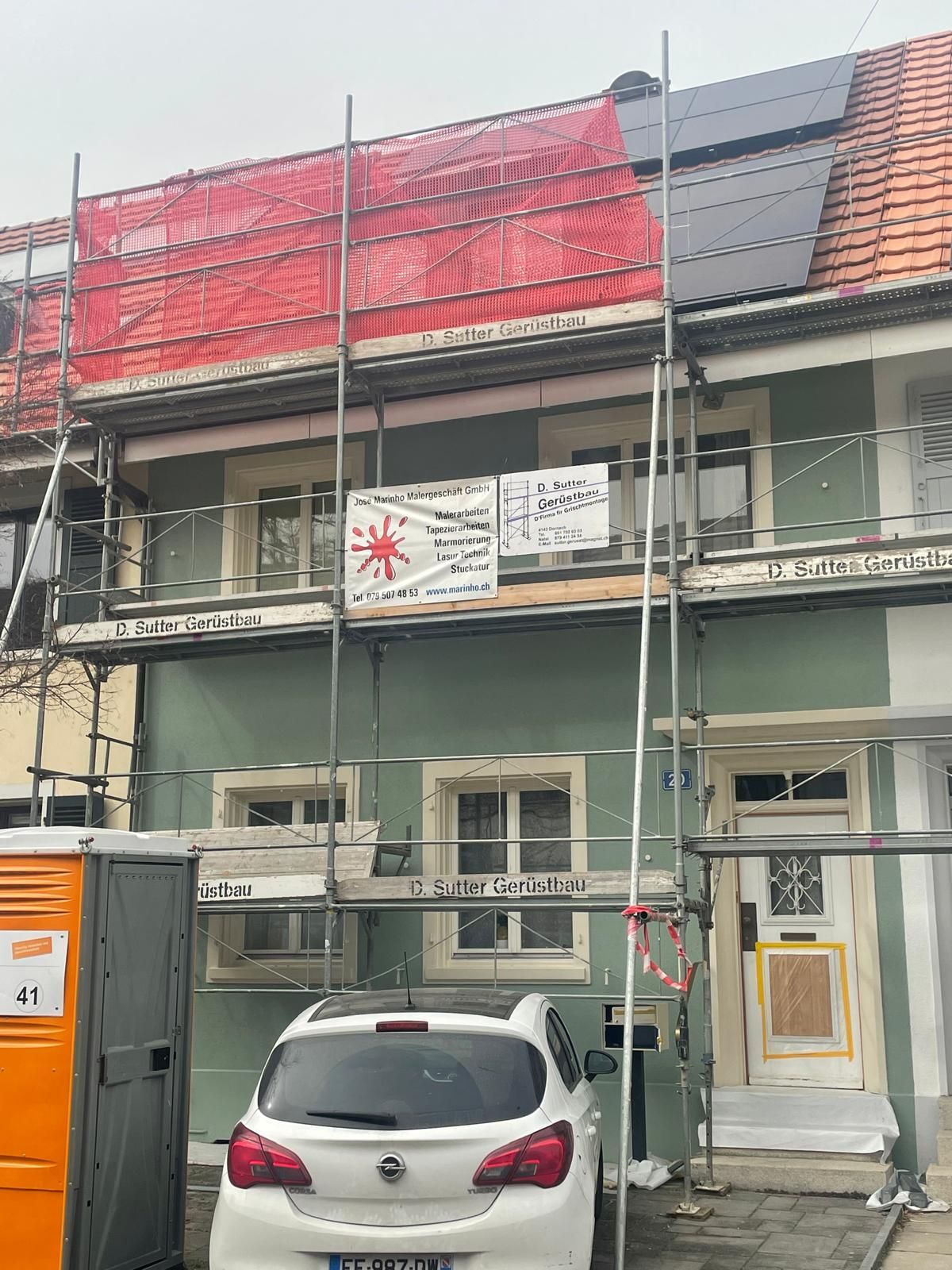 Mit einem Pinsel wird weisse Farbe an die Kante einer Wandleiste vor einer hellgrauen Wand aufgetragen.