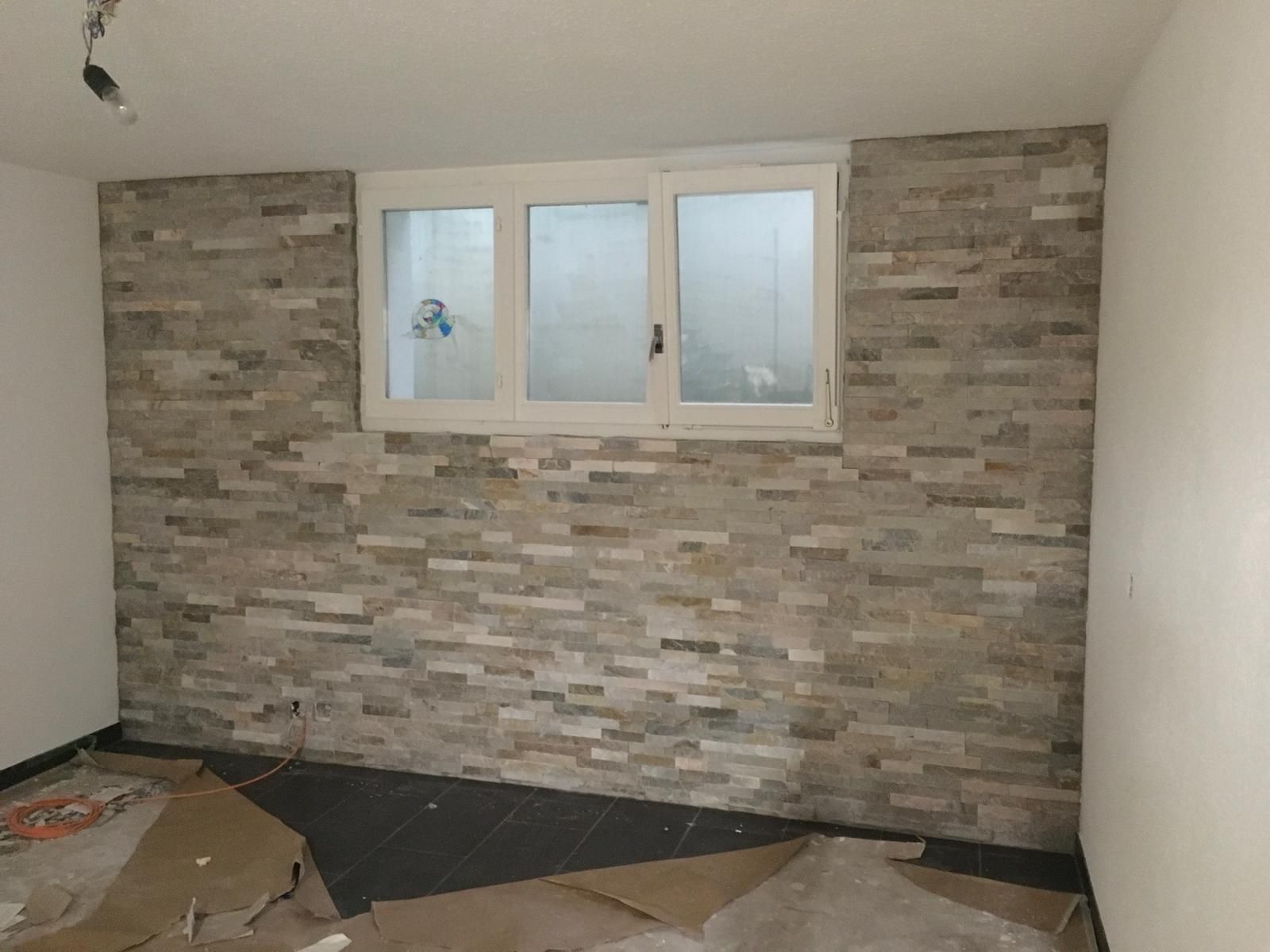 Mit einem Pinsel wird weisse Farbe an die Kante einer Wandleiste vor einer hellgrauen Wand aufgetragen.