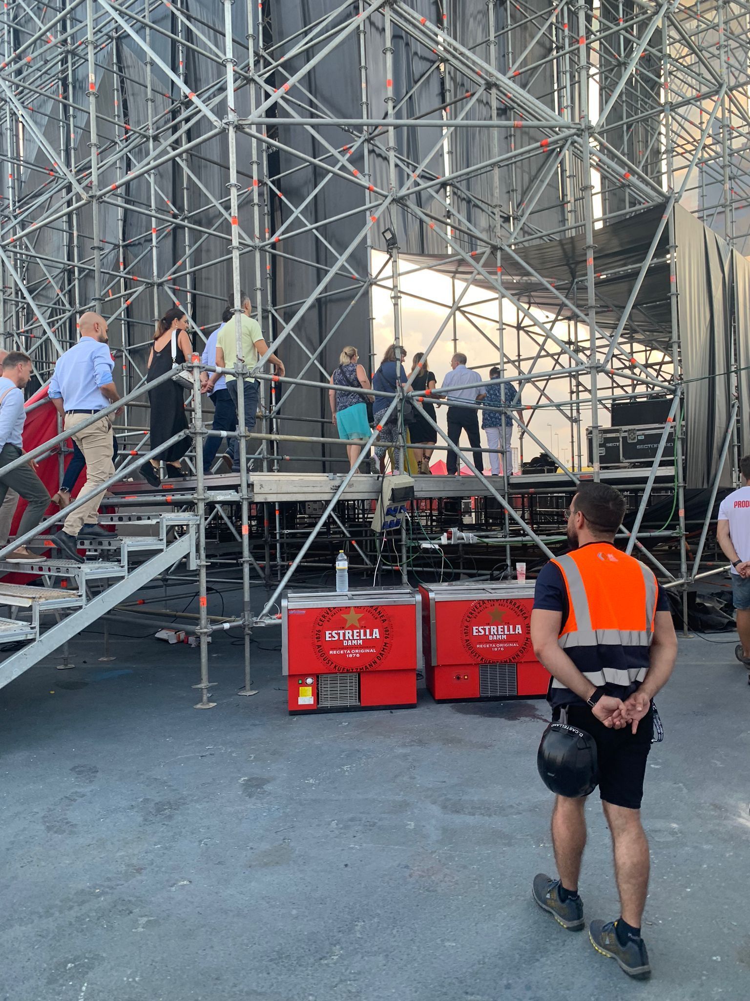 Un hombre con un chaleco naranja está parado frente a una gran estructura de andamios.