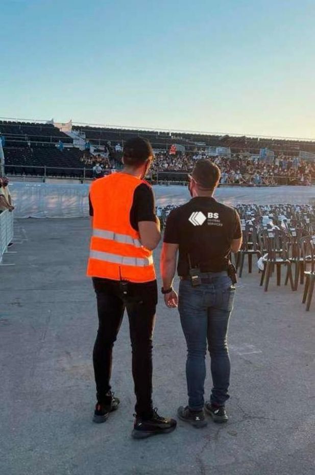 Un hombre con un chaleco naranja está de pie junto a otro hombre con una camisa negra.