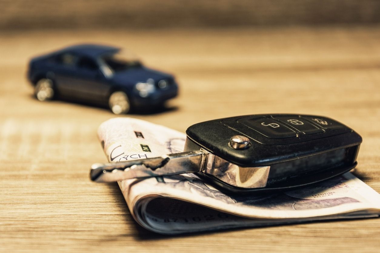 Llave de coche sobre dinero con un coche de juguete de fondo.