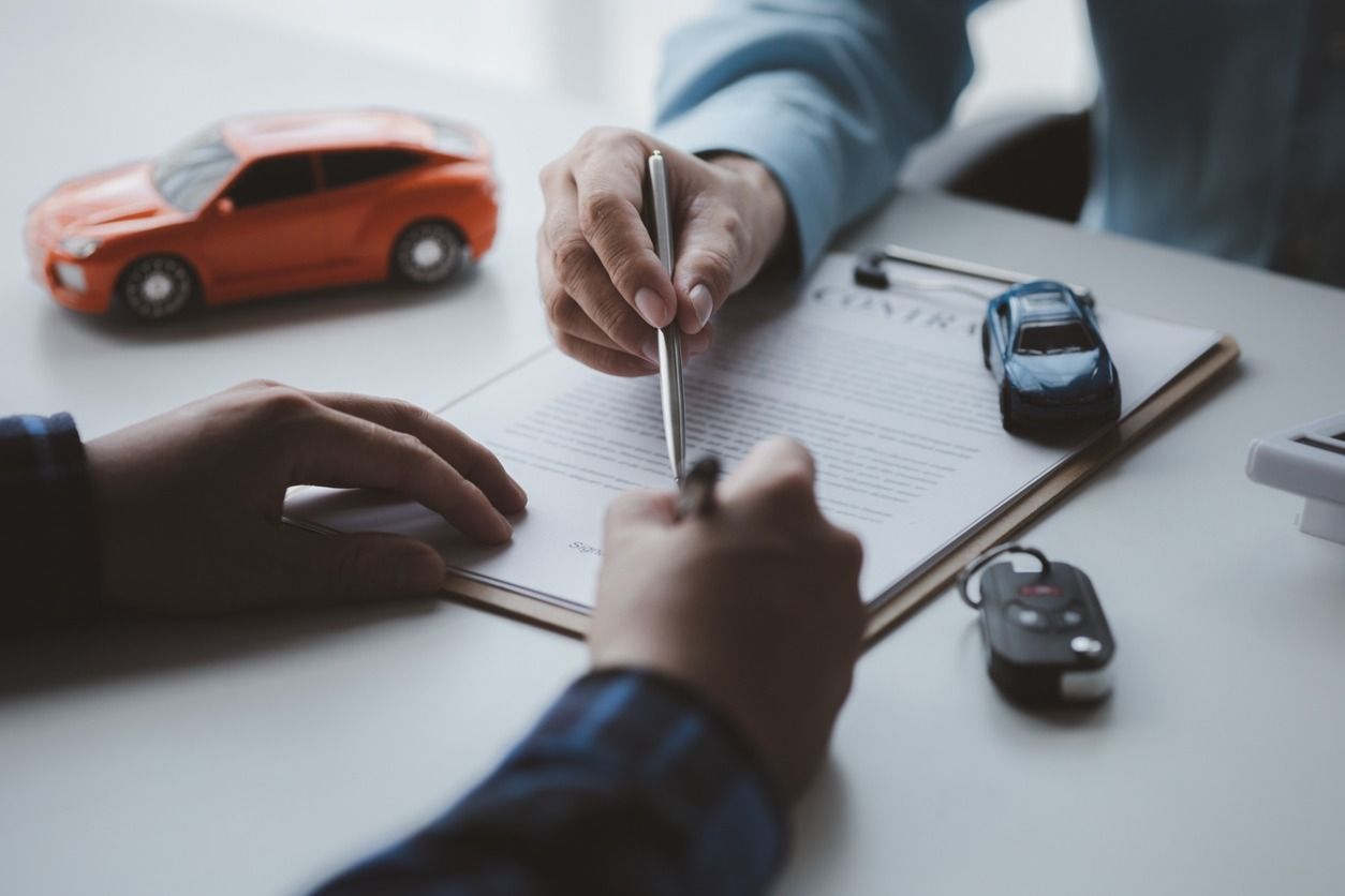 Dos personas firmando un contrato de compra de un automóvil, pequeños modelos de automóviles sobre una mesa.