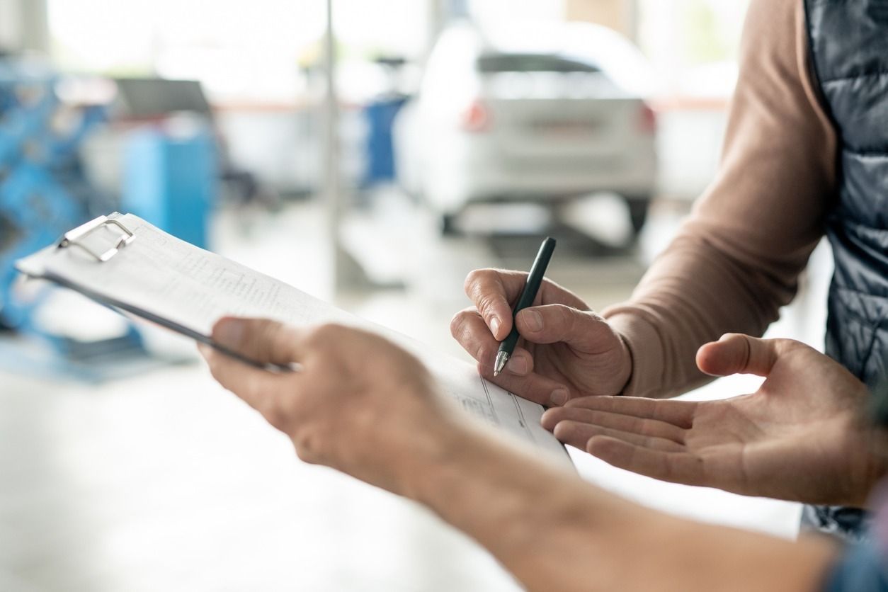 Mecánico firmando un documento en un portapapeles; en un garaje.