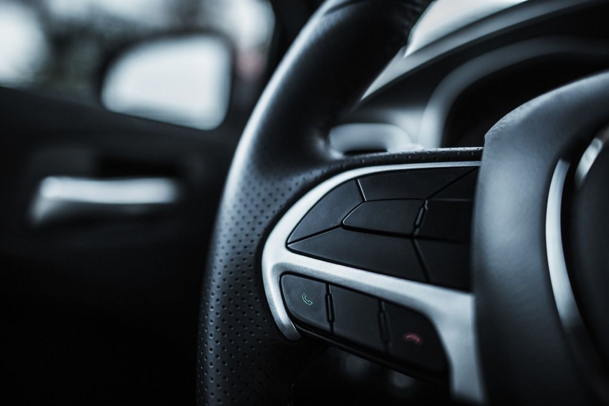 Primer plano de un volante de automóvil negro con controles, detalles grises y cuero perforado.