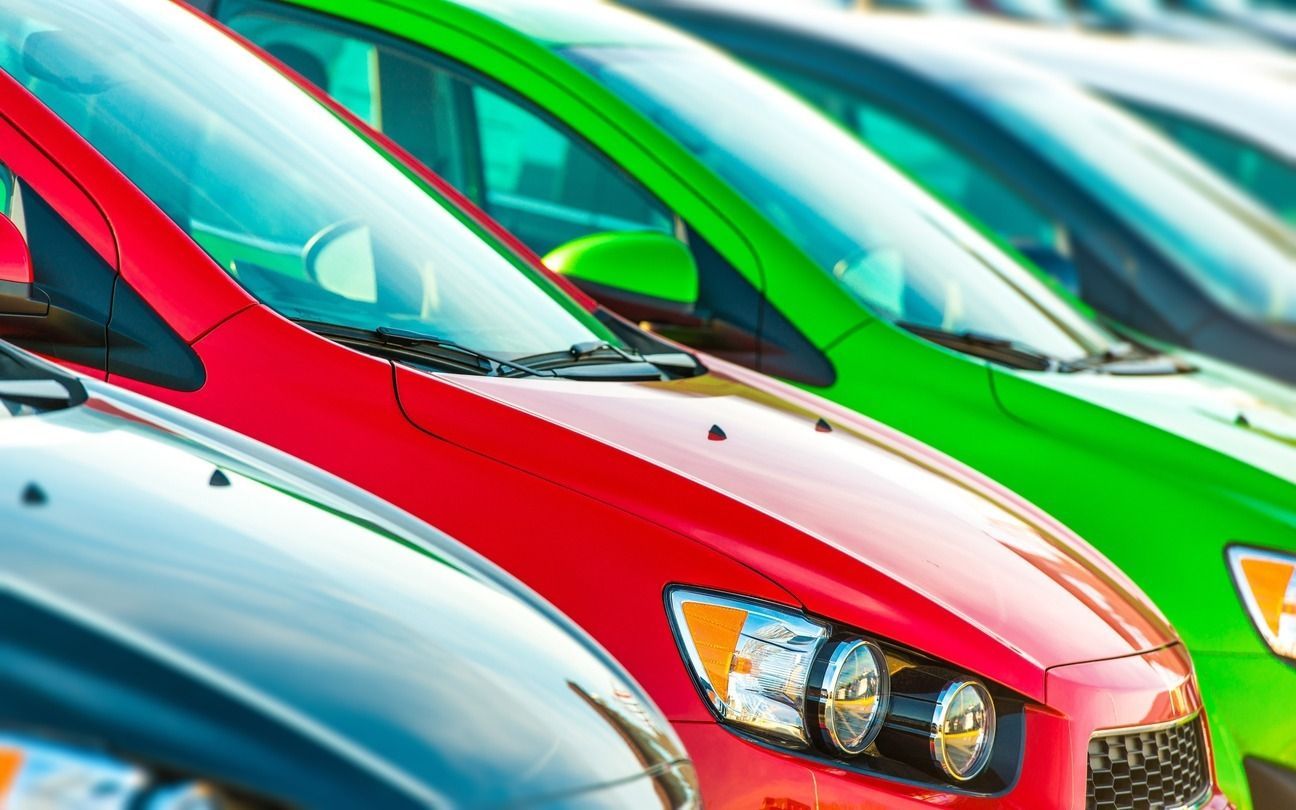 Fila de coches coloridos aparcados afuera, incluidos rojos y verdes.