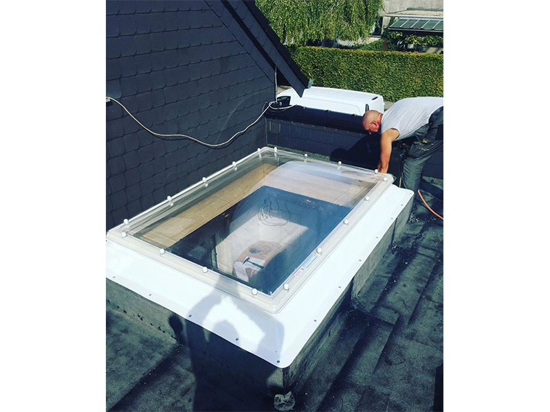 Ein Mann arbeitet an einem Oberlicht auf dem Dach eines Gebäudes.