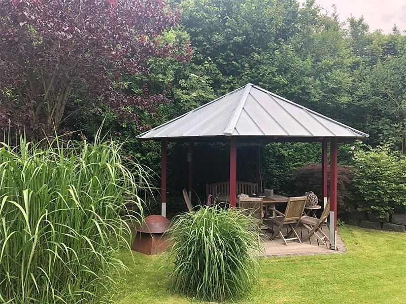 Ein Pavillon mit Tisch und Stühlen inmitten eines üppig grünen Gartens.