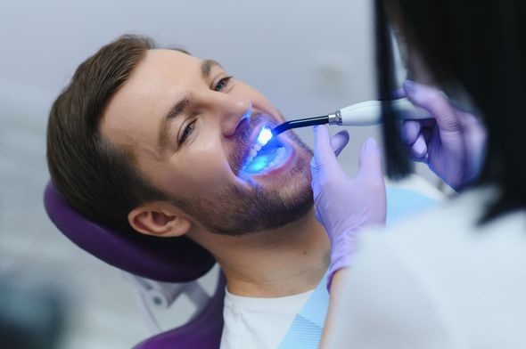 Ein Zahnarzt verwendet während einer zahnärztlichen Behandlung in einer Klinik blaues Licht auf den Zähnen des Patienten.