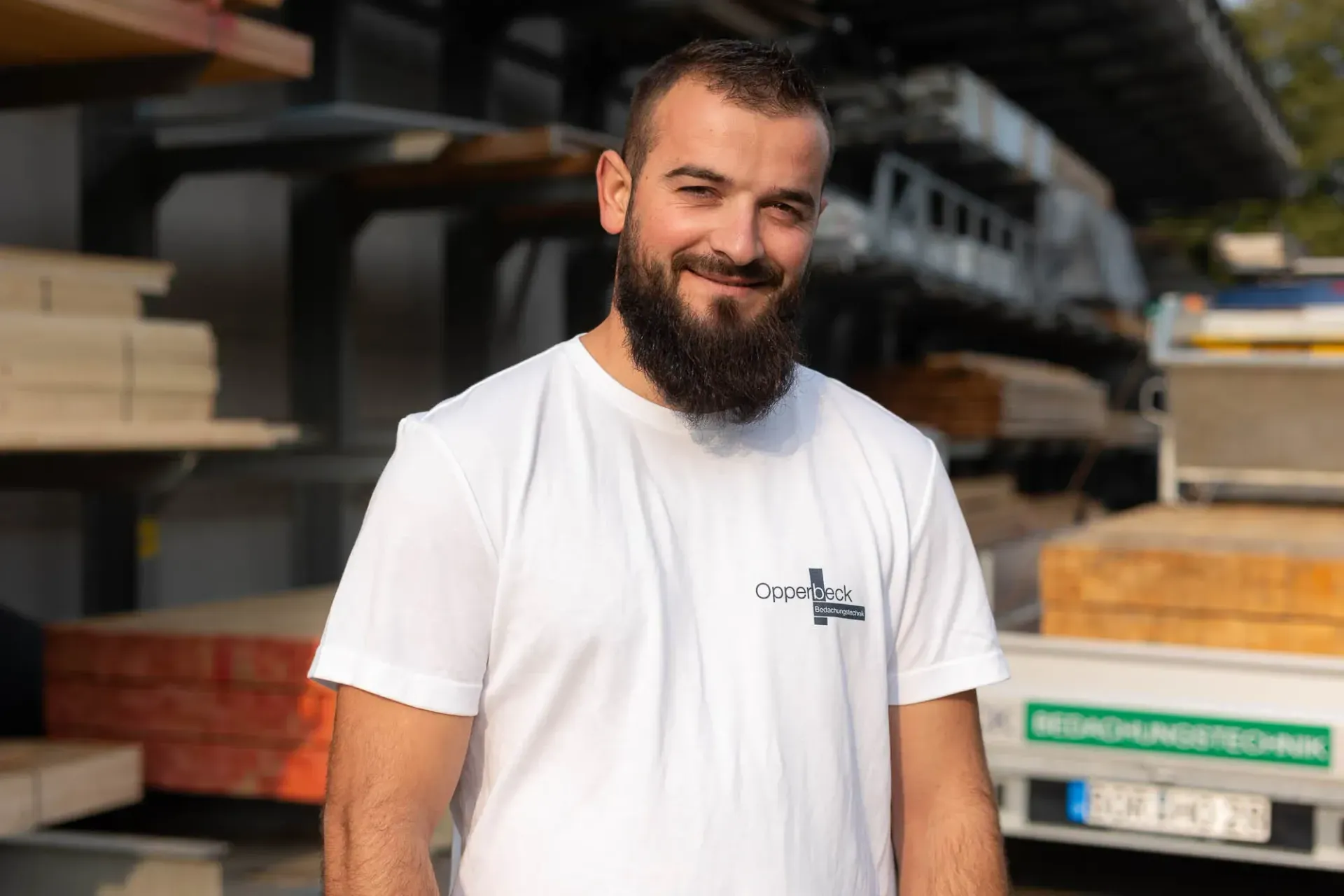 Ein Mann mit Bart und weißem T-Shirt steht vor einer Lagerhalle.