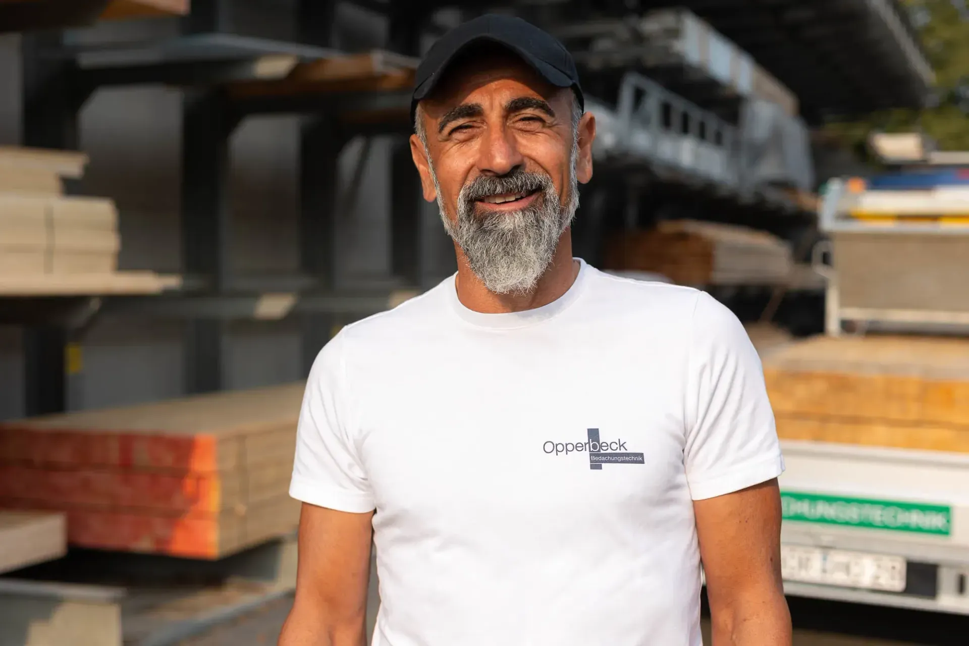 Ein Mann mit Bart trägt ein weißes T-Shirt und einen schwarzen Hut.