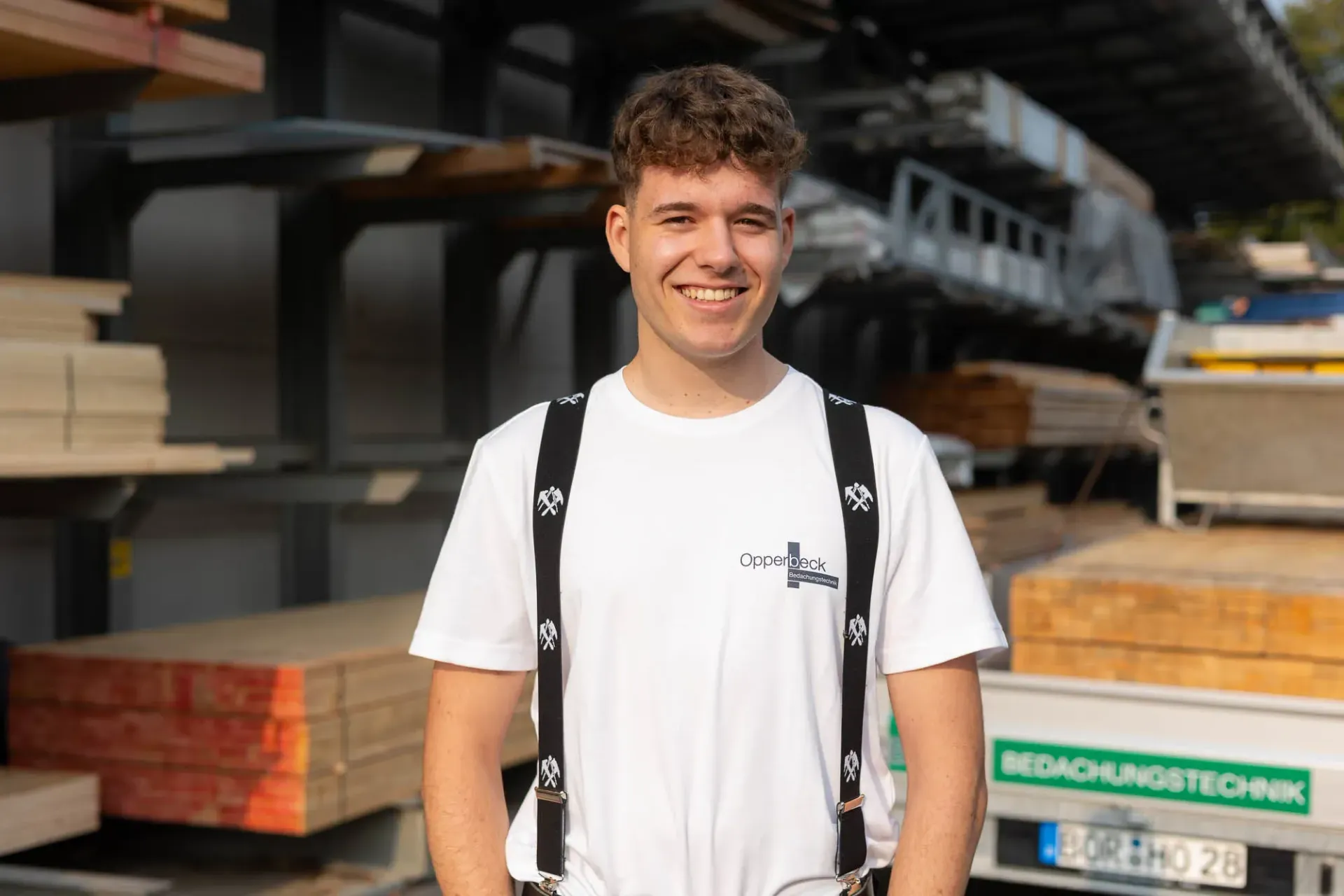 Ein junger Mann mit Hosenträgern und weißem Hemd steht vor einer Lagerhalle.