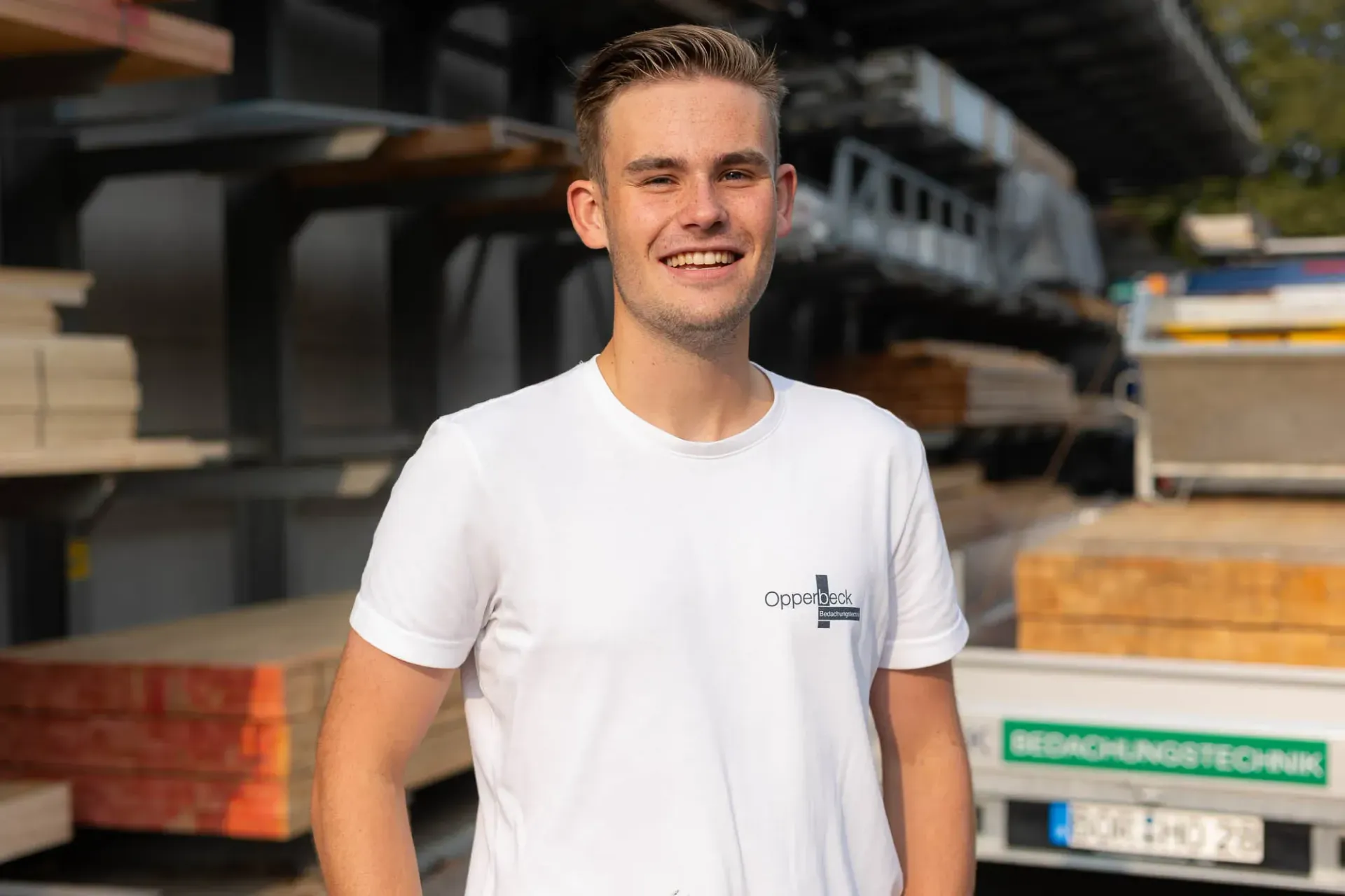 Ein junger Mann in einem weißen T-Shirt steht vor einem Lastwagen.