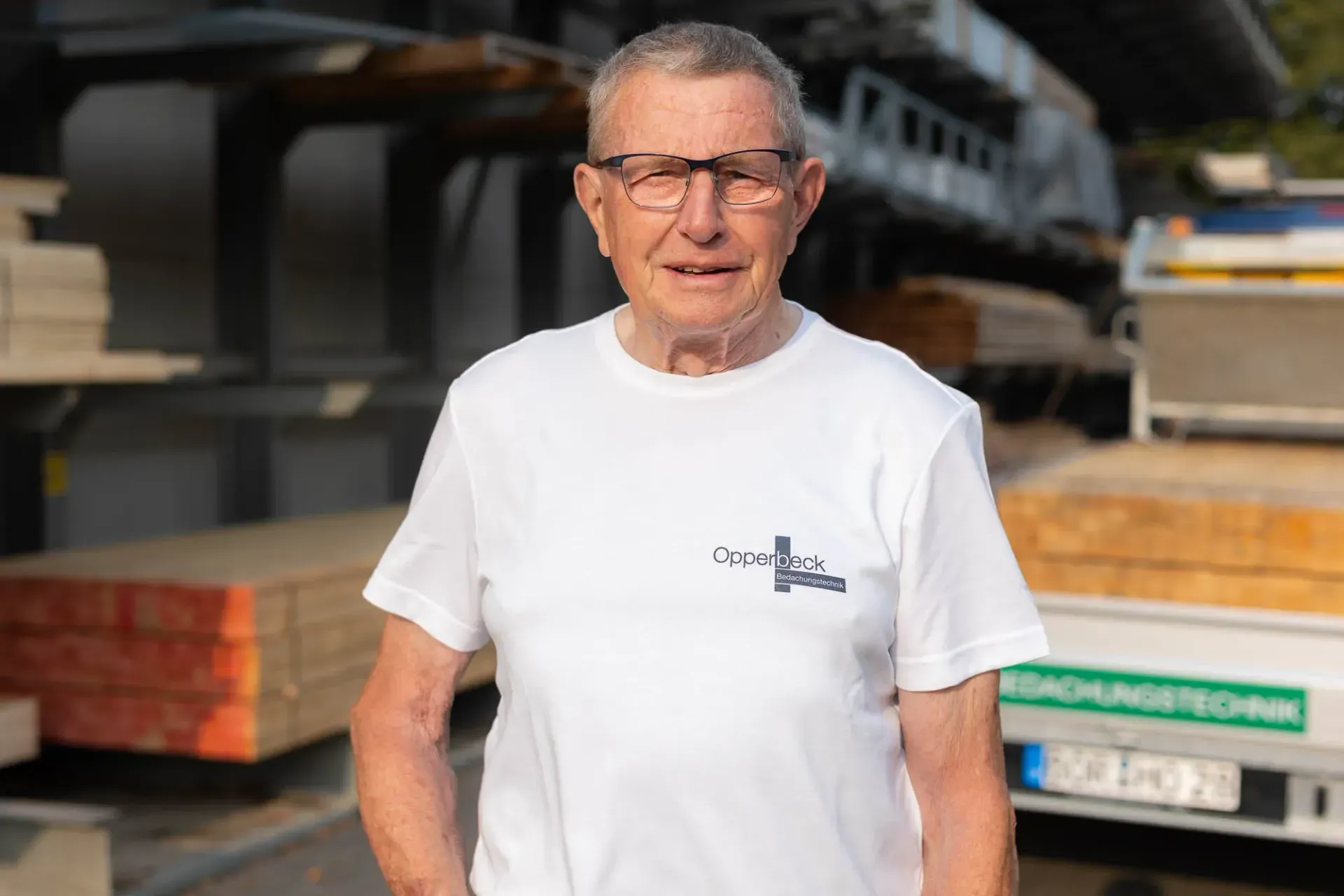 Ein Mann mit Brille und weißem Hemd steht vor einem mit Holz beladenen Lastwagen.