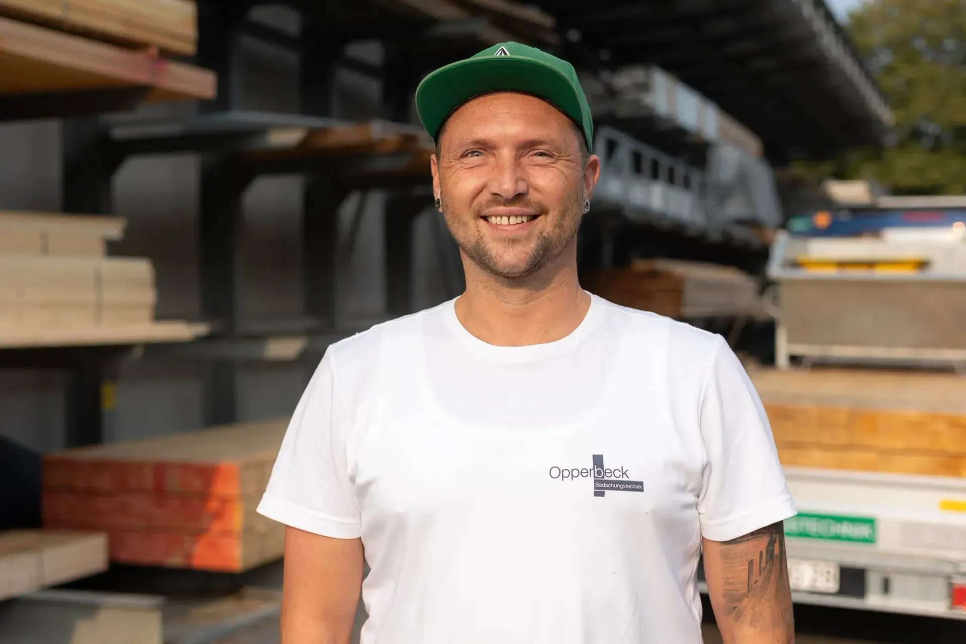Ein Mann mit grünem Hut und weißem T-Shirt steht vor einer Lagerhalle.