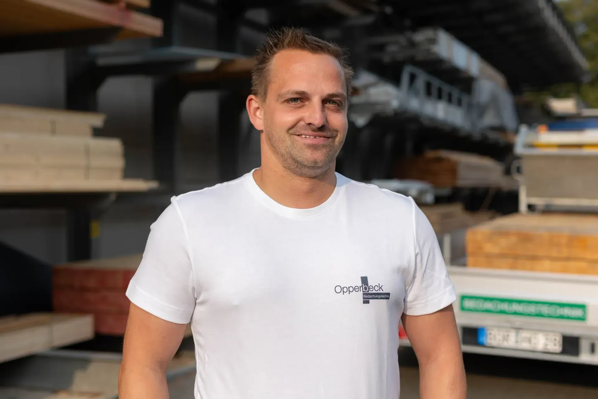 Ein Mann in einem weißen T-Shirt steht vor einer Lagerhalle.