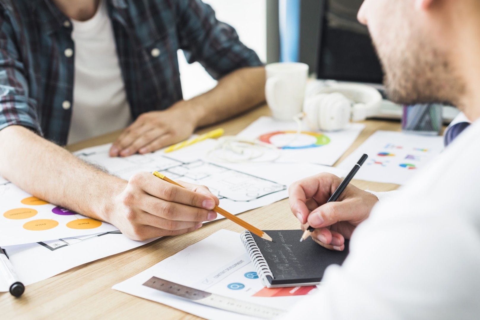 Dos personas revisan gráficos y tablas sobre un escritorio durante una reunión de negocios.