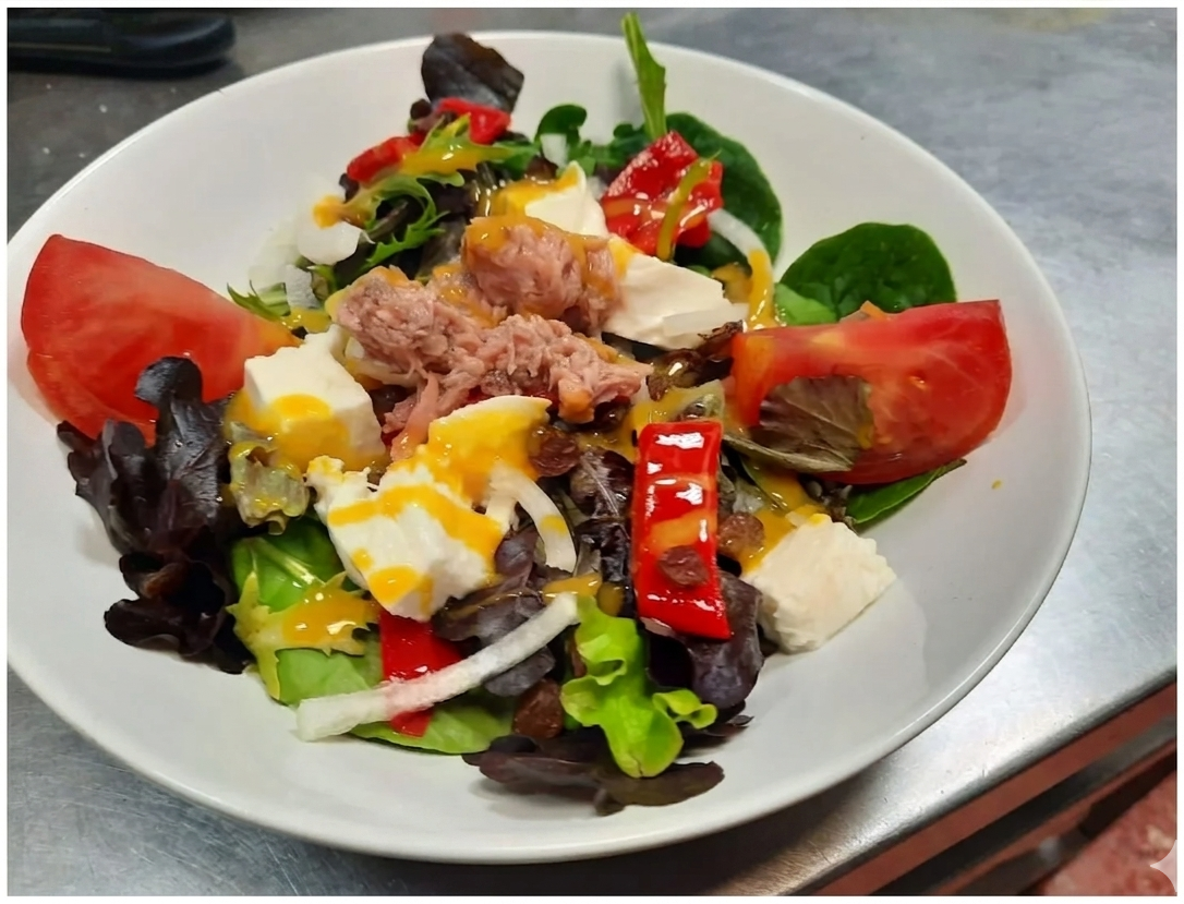 Ensalada colorida con atún, tomates, verduras, huevo y pimiento rojo en un plato blanco.